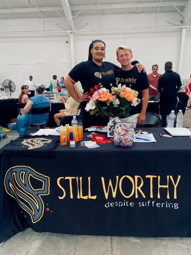 Two people behind a Still Worthy banner table at a community event